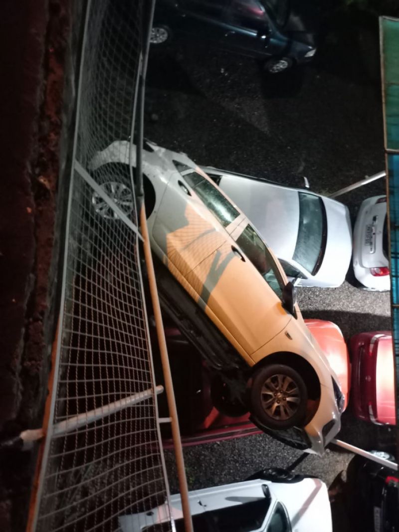 Carro cai em cima de veículos ao despencar de muro